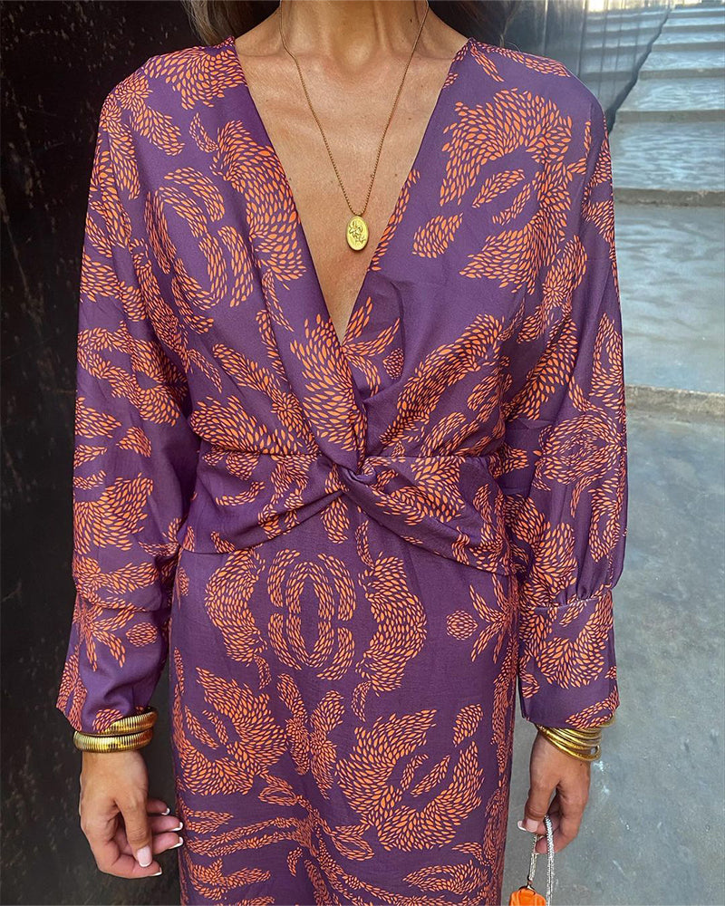 Abito elegante viola con motivo arancione, scollatura a V profonda, maniche lunghe, accessori dorati. Moda femminile, stile sofisticato.