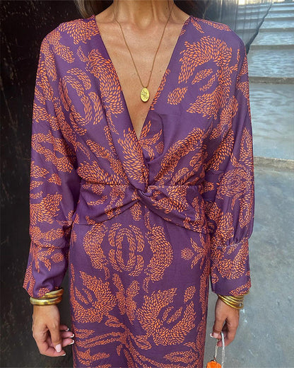 Abito elegante viola con motivo arancione, scollatura a V profonda, maniche lunghe, accessori dorati. Moda femminile, stile sofisticato.