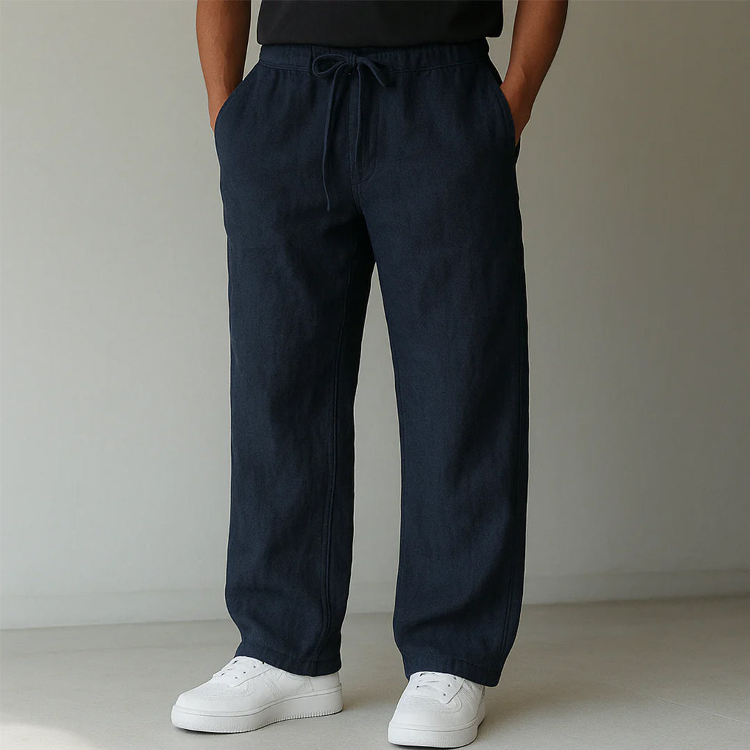 Pantaloni larghi blu scuro in lino, indossati con scarpe da ginnastica bianche. Stile casual, moda uomo, abbigliamento estivo.