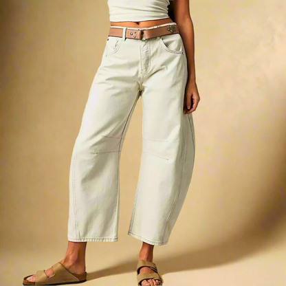 Donna in pantaloni bianchi larghi, cintura marrone, sandali beige. Moda casual, abbigliamento estivo, stile rilassato. Sfondo beige.