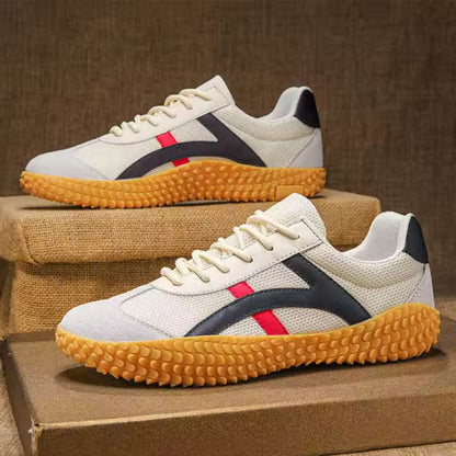 Scarpe da ginnastica bianche con suola in gomma gialla, dettagli blu e rossi, su sfondo di tessuto marrone. Design sportivo e moderno.