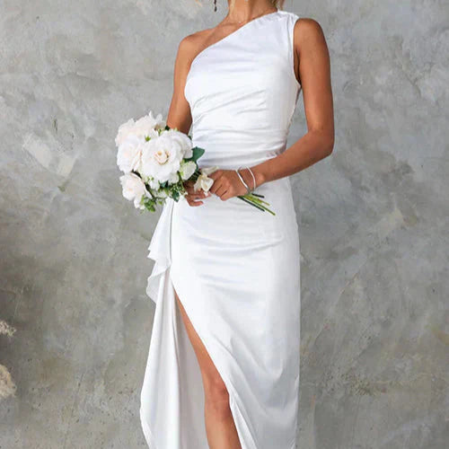 Abito da sposa bianco monospalla con spacco laterale, bouquet di rose bianche, sfondo grigio. Elegante e moderno, perfetto per matrimoni.