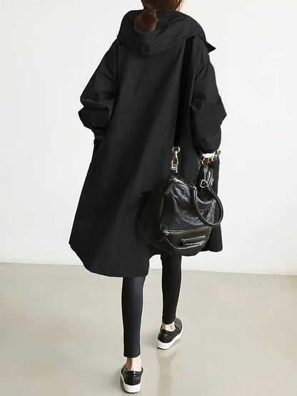 Donna di spalle con cappotto nero oversize, leggings e borsa a tracolla in pelle. Moda casual autunnale, stile urbano minimalista.