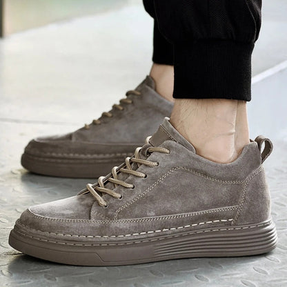 Scarpe da ginnastica uomo in pelle scamosciata grigia, suola spessa, design casual, indossate con pantaloni sportivi neri.