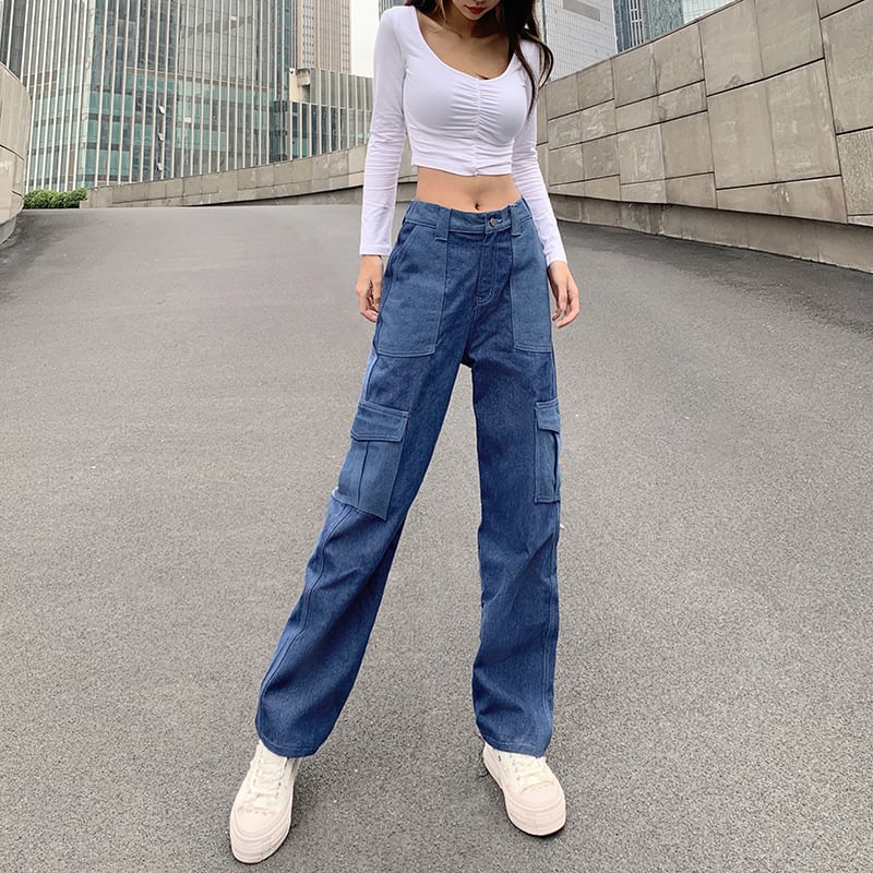 Donna in jeans cargo blu e top bianco su strada urbana. Moda casual, pantaloni larghi, tendenza streetwear, abbigliamento femminile moderno.