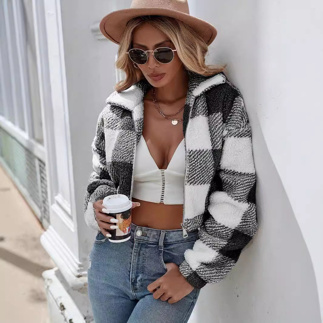 Donna con giacca a quadri bianca e nera, cappello beige, occhiali da sole, top bianco e jeans, tiene un caffè. Moda autunnale casual chic.