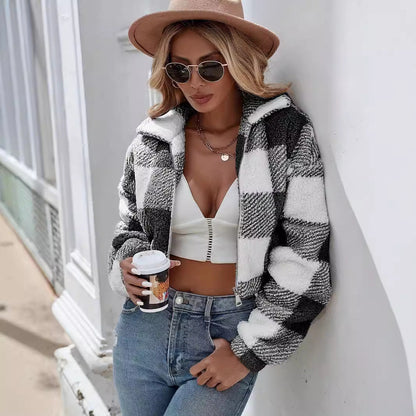 Donna con giacca a quadri bianca e nera, cappello beige, occhiali da sole, top bianco e jeans, tiene un caffè. Moda autunnale casual chic.