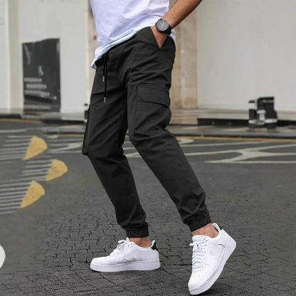 Uomo con pantaloni cargo neri e sneakers bianche su strada urbana. Moda casual maschile, stile streetwear, abbigliamento moderno.