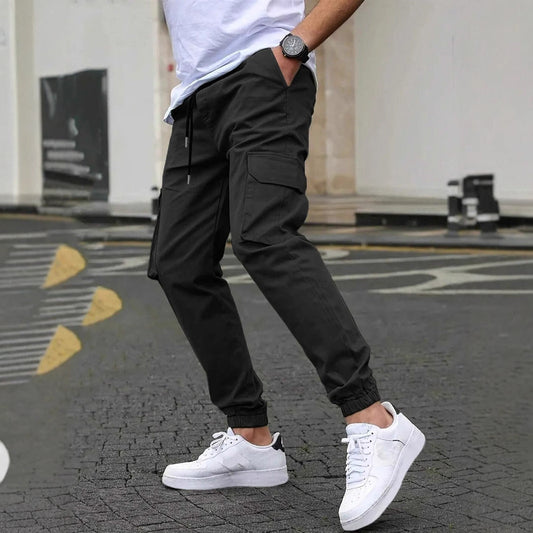 Uomo con pantaloni cargo neri e sneakers bianche su strada urbana. Moda casual maschile, stile streetwear, abbigliamento moderno.