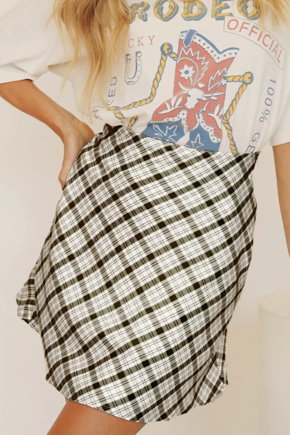 Donna con maglietta grafica rodeo e gonna a quadri bianca e nera. Moda casual, abbigliamento estivo, stile giovanile.