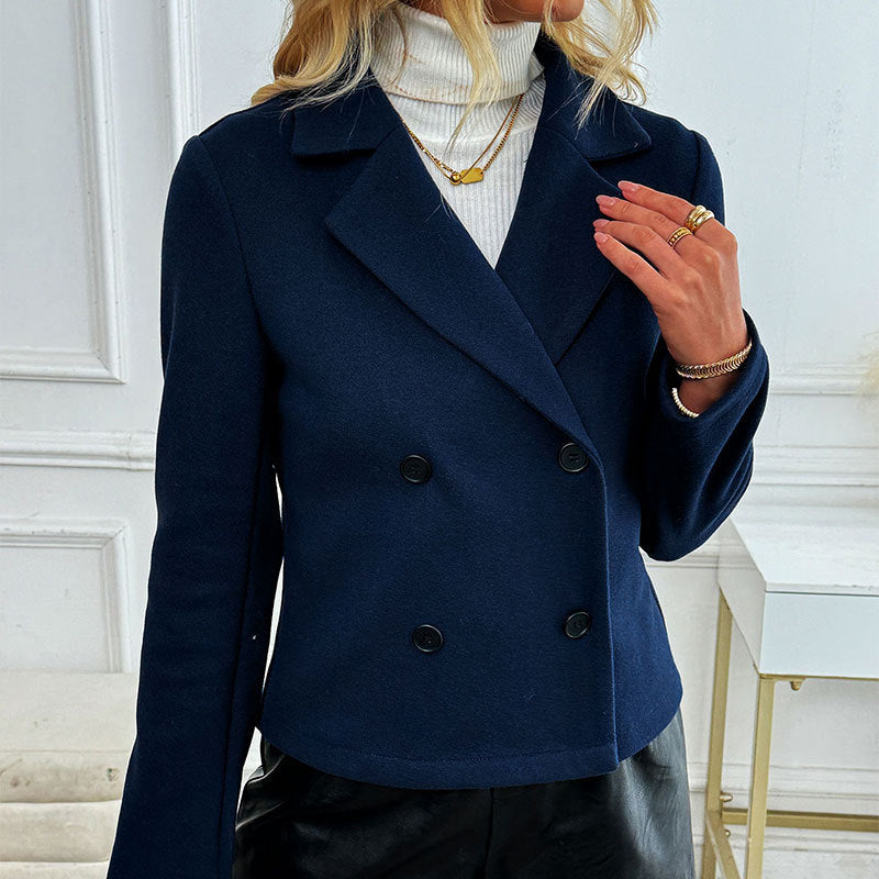 Giacca blu doppiopetto elegante su donna con maglione bianco a collo alto, accessori dorati, sfondo interno minimalista. Moda autunno inverno.