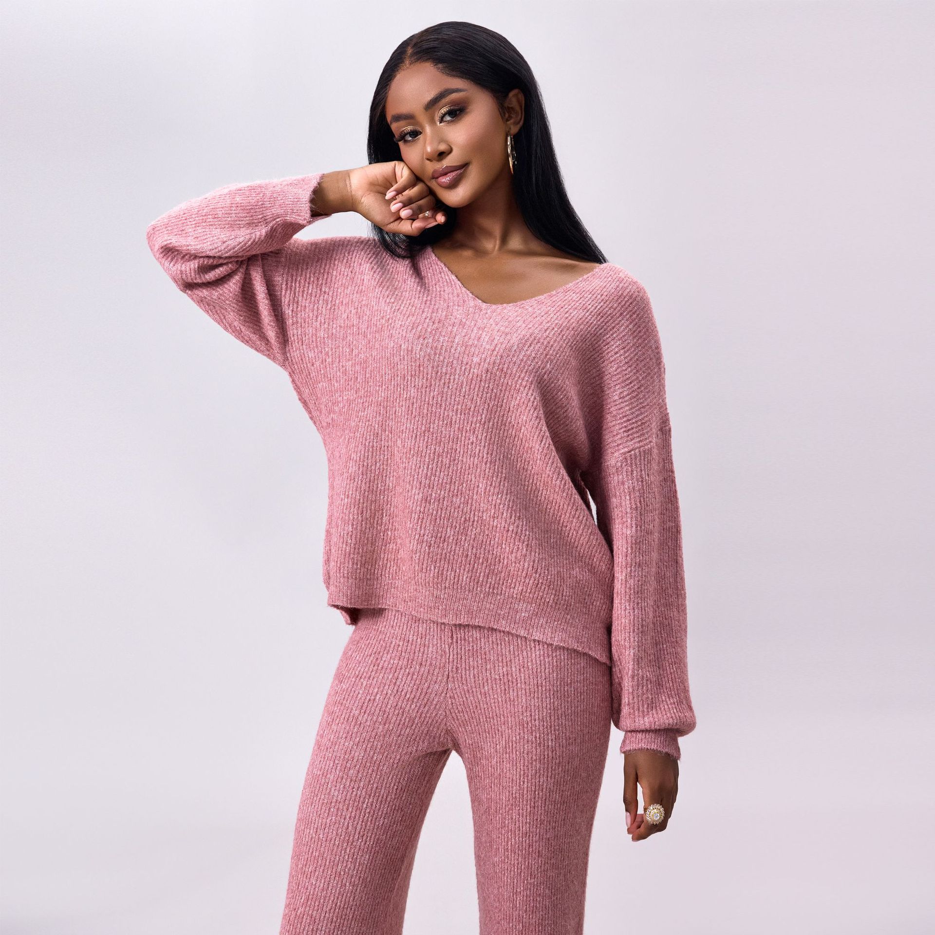 Donna con maglione e pantaloni rosa in maglia, posa elegante su sfondo neutro. Moda autunno inverno, abbigliamento casual chic, tendenze 2023.