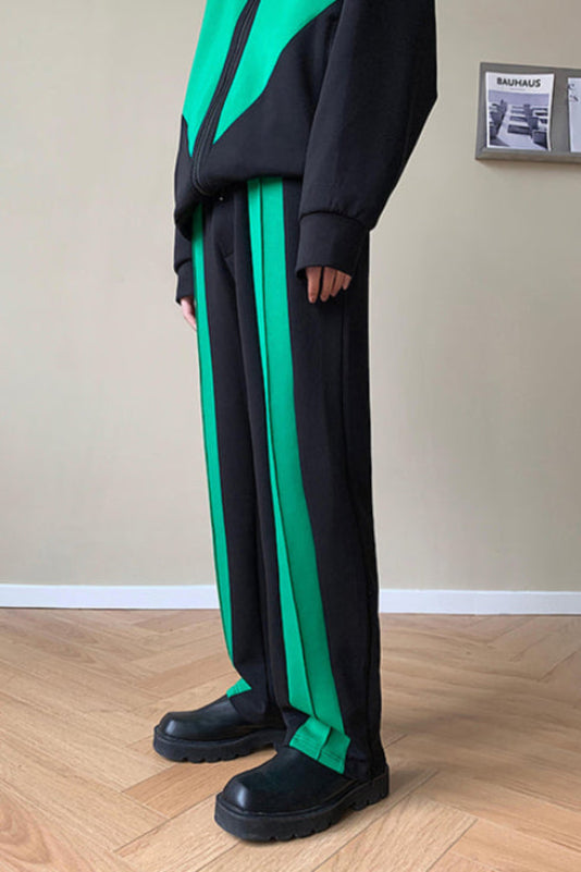 Pantaloni sportivi neri e verdi, design moderno, indossati con giacca abbinata. Moda casual, pavimento in legno, rivista Bauhaus sullo sfondo.
