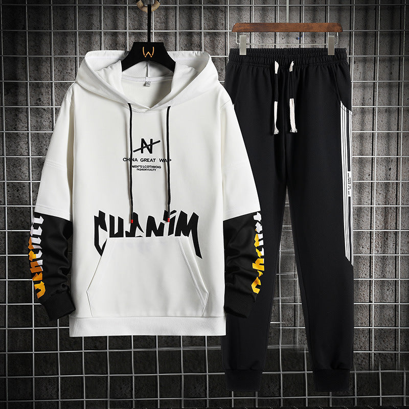 Set tuta sportiva uomo, felpa bianca con cappuccio e scritte nere, pantaloni neri con strisce laterali bianche, appeso su griglia metallica.