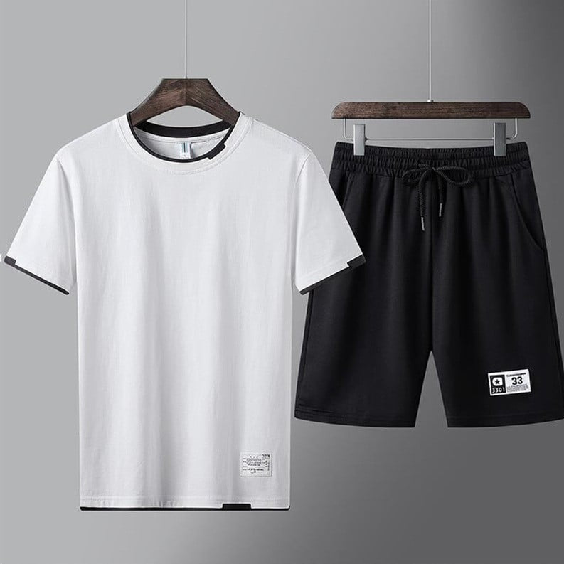 Completo sportivo uomo, t-shirt bianca e pantaloncini neri, appesi su grucce. Abbigliamento casual estivo, moda maschile, stile minimalista.