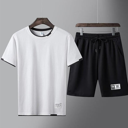 Completo sportivo uomo, t-shirt bianca e pantaloncini neri, appesi su grucce. Abbigliamento casual estivo, moda maschile, stile minimalista.