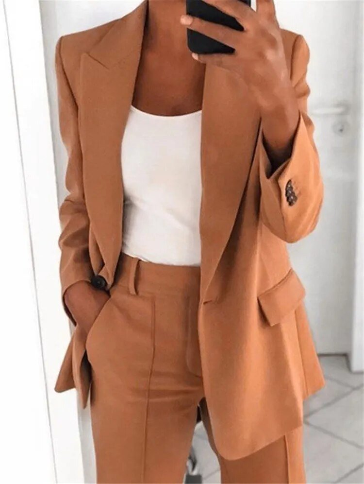 Completo donna elegante color cammello, giacca e pantaloni abbinati, indossato con top bianco. Moda femminile, abbigliamento formale chic.