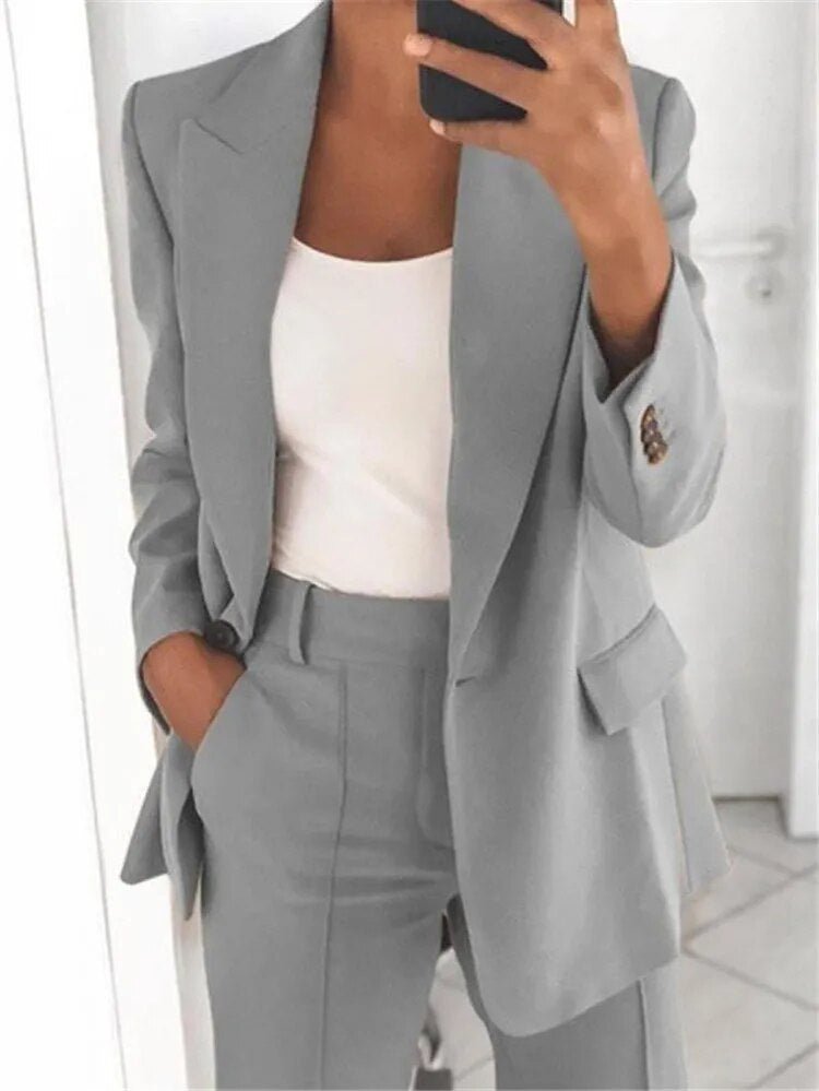 Donna in abito grigio elegante, giacca e pantaloni coordinati, con top bianco. Moda business casual, outfit professionale per ufficio.