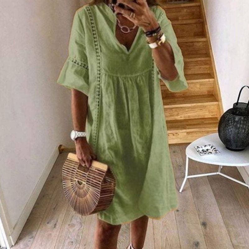 Donna con abito verde estivo, borsa di legno a mezzaluna, in piedi su pavimento in legno chiaro, scala in legno sullo sfondo.