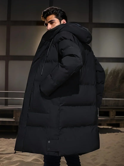 Giovane uomo con cappotto invernale nero imbottito, cappuccio, in piedi su una spiaggia di sera. Moda maschile, abbigliamento invernale elegante.