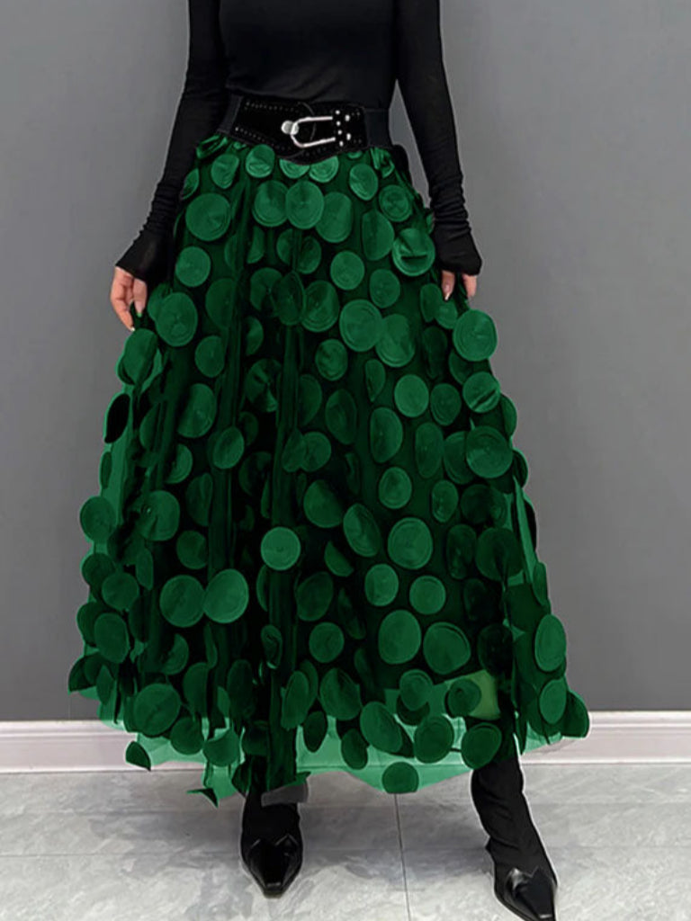 Gonna lunga verde con cerchi decorativi, cintura nera, indossata con maglia nera a maniche lunghe. Moda femminile elegante e moderna.