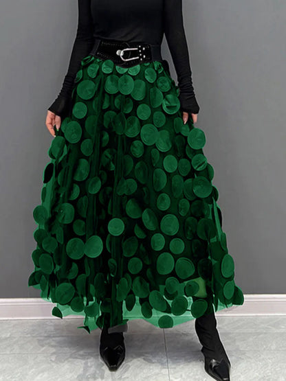 Gonna lunga verde con cerchi decorativi, cintura nera, indossata con maglia nera a maniche lunghe. Moda femminile elegante e moderna.