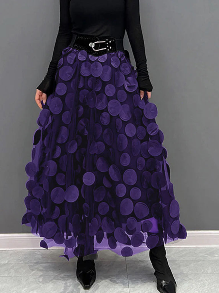 Gonna lunga viola con cerchi in rilievo, cintura nera, indossata con maglia nera a maniche lunghe. Moda femminile elegante e moderna.