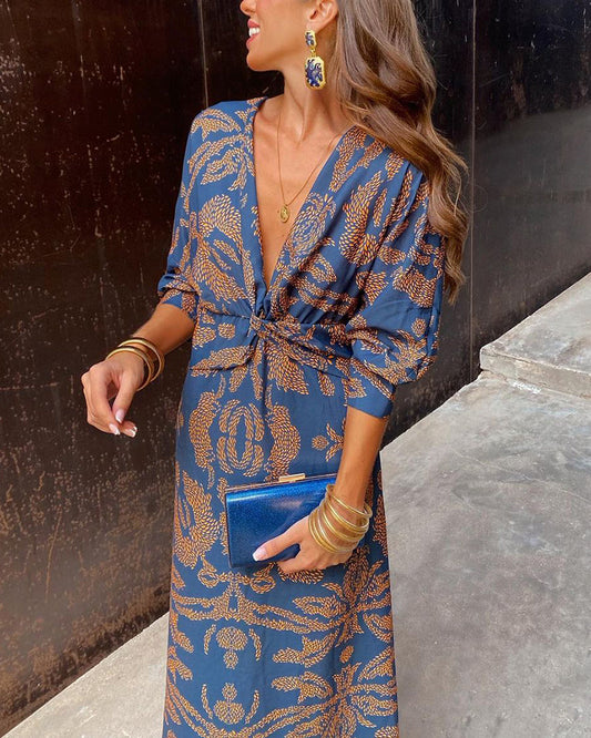 Donna con abito lungo blu a motivi dorati, orecchini pendenti, bracciali dorati e pochette blu. Moda elegante, stile sofisticato, accessori chic.