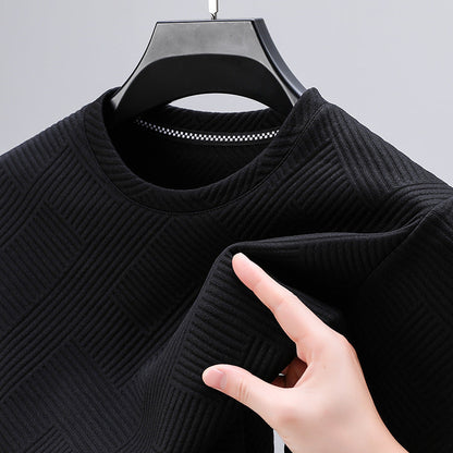Maglia nera a maniche lunghe con motivo geometrico, tessuto a coste, su appendiabiti. Mano che tocca il tessuto. Moda uomo, abbigliamento casual.