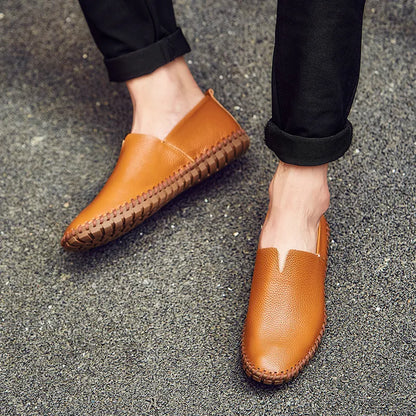 Scarpe mocassini in pelle marrone chiaro su strada asfaltata, indossate con pantaloni neri. Calzature eleganti uomo, moda casual, comfort quotidiano.