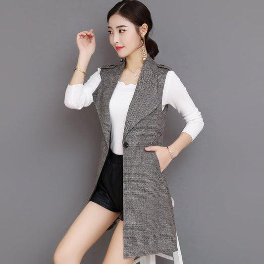 Donna in posa con gilet lungo grigio a quadri, maglia bianca e pantaloncini neri. Moda autunnale elegante, abbigliamento casual chic.