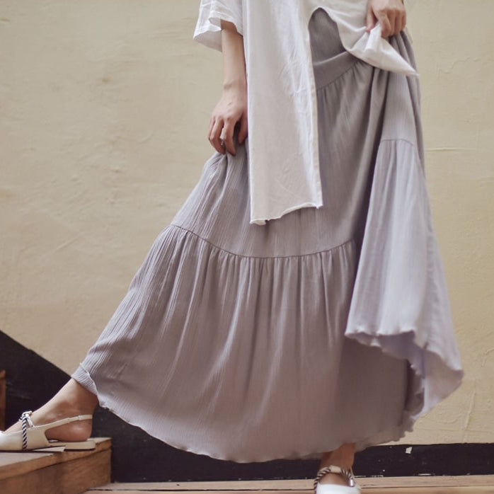 Donna in abito lungo grigio chiaro, tessuto plissettato, cammina su scale interne. Moda casual, eleganza quotidiana, stile estivo.