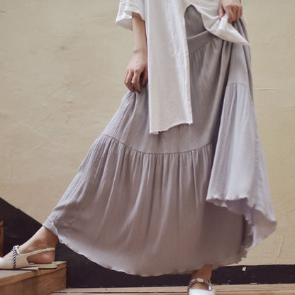 Donna in abito lungo grigio chiaro, tessuto plissettato, cammina su scale interne. Moda casual, eleganza quotidiana, stile estivo.