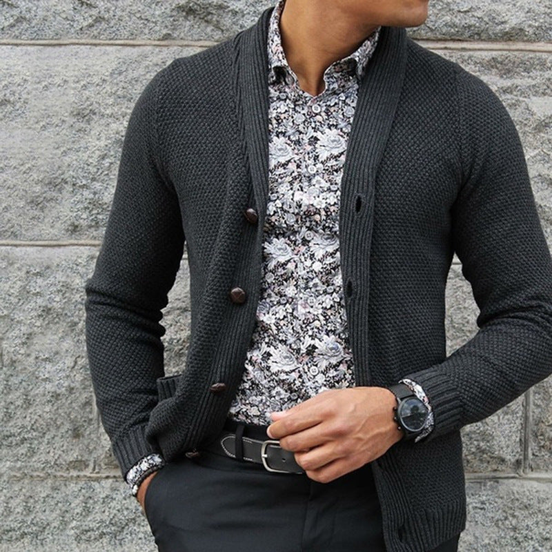 Uomo con cardigan grigio scuro, camicia a fiori bianca e nera, pantaloni neri. Moda maschile elegante, stile autunnale, outfit casual chic.