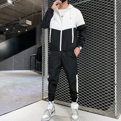 Uomo in tuta sportiva bianca e nera, scarpe da ginnastica grigie, posa in un ambiente industriale moderno. Abbigliamento casual, moda streetwear.