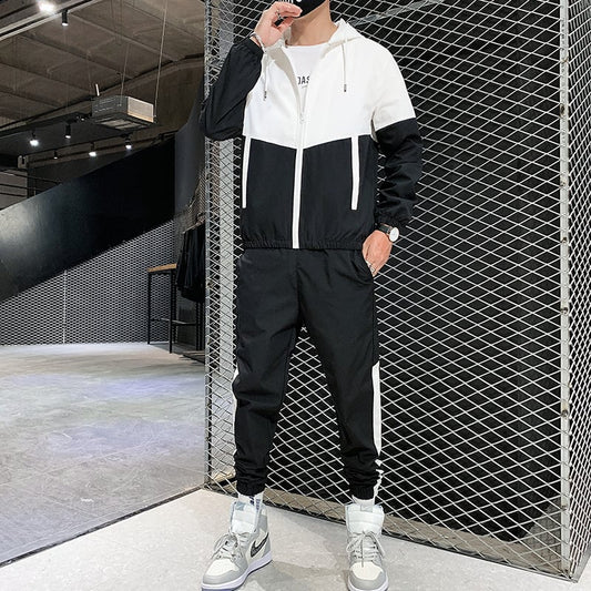 Uomo in tuta sportiva bianca e nera, scarpe da ginnastica grigie, posa in un ambiente industriale moderno. Abbigliamento casual, moda streetwear.