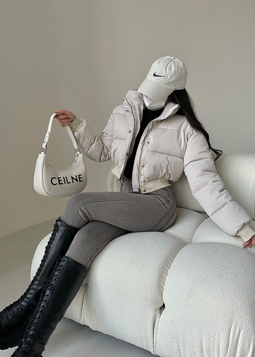 Donna con giacca imbottita bianca, cappello da baseball e borsa a spalla su divano moderno. Moda invernale, stile casual chic, tendenze 2023.