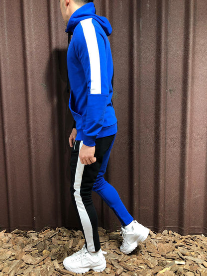 Uomo in tuta sportiva blu con strisce bianche, scarpe da ginnastica bianche, cammina su terreno di corteccia. Moda casual, abbigliamento sportivo.