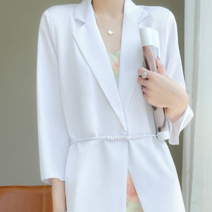 Donna in giacca bianca elegante, tiene una rivista. Moda femminile, abbigliamento formale, stile sofisticato. Accessori minimalisti.