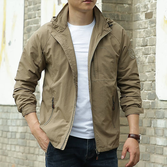 Giacca casual beige da uomo, stile sportivo, con zip e tasche, indossata su maglietta bianca e jeans. Look urbano, moda maschile autunnale.