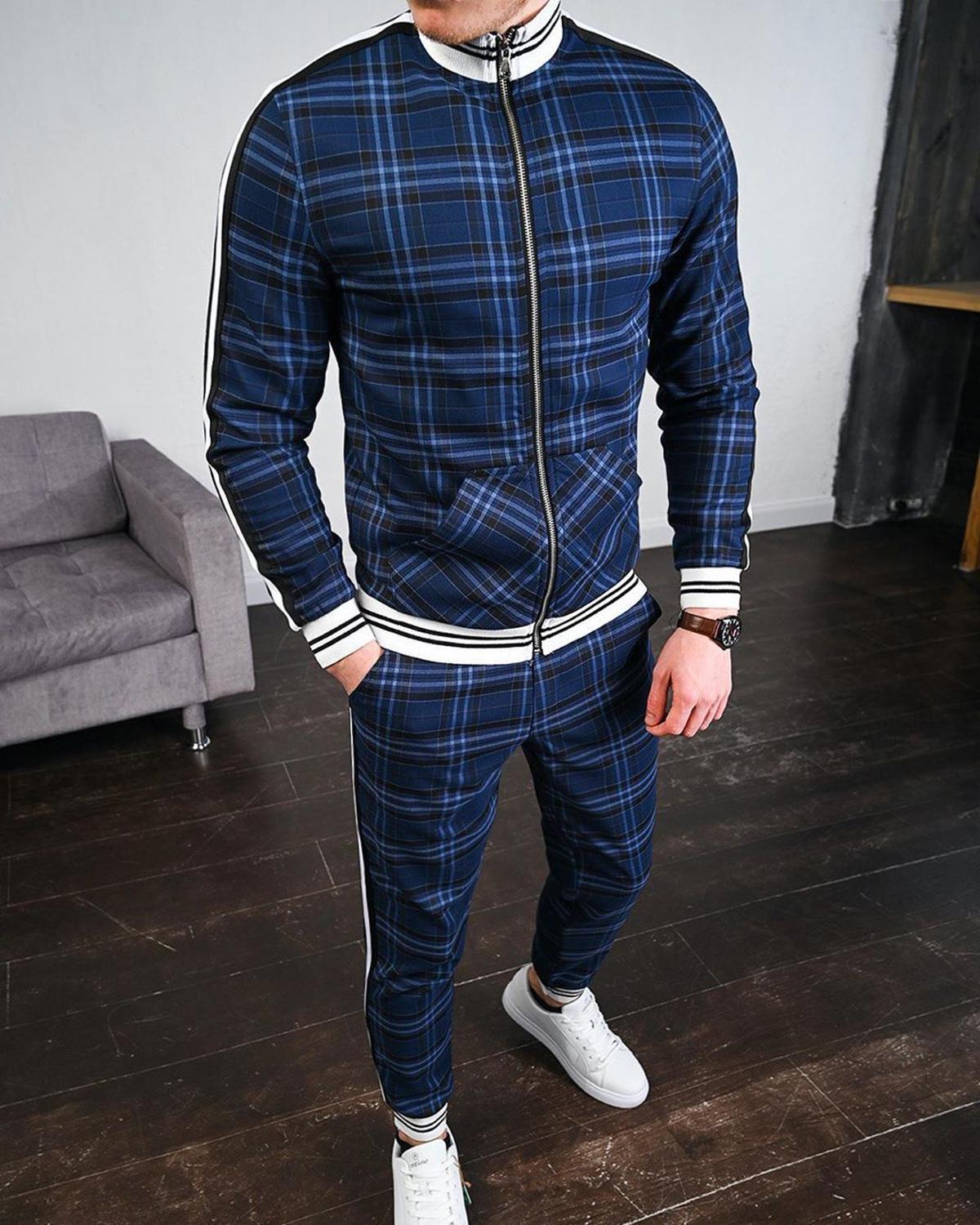 Uomo in tuta sportiva a quadri blu, con scarpe bianche, in piedi su pavimento in legno. Stile casual, moda maschile, abbigliamento moderno.