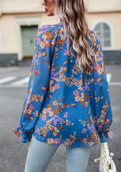 Donna di spalle con camicetta floreale blu e jeans chiari, capelli ondulati biondi. Moda casual femminile, abbigliamento primaverile, stile urbano.