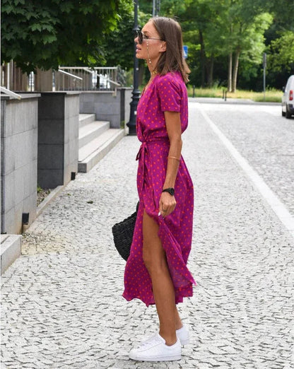 Donna in abito rosa a pois, occhiali da sole, borsa nera, scarpe da ginnastica bianche, cammina su strada lastricata, estate, moda casual.
