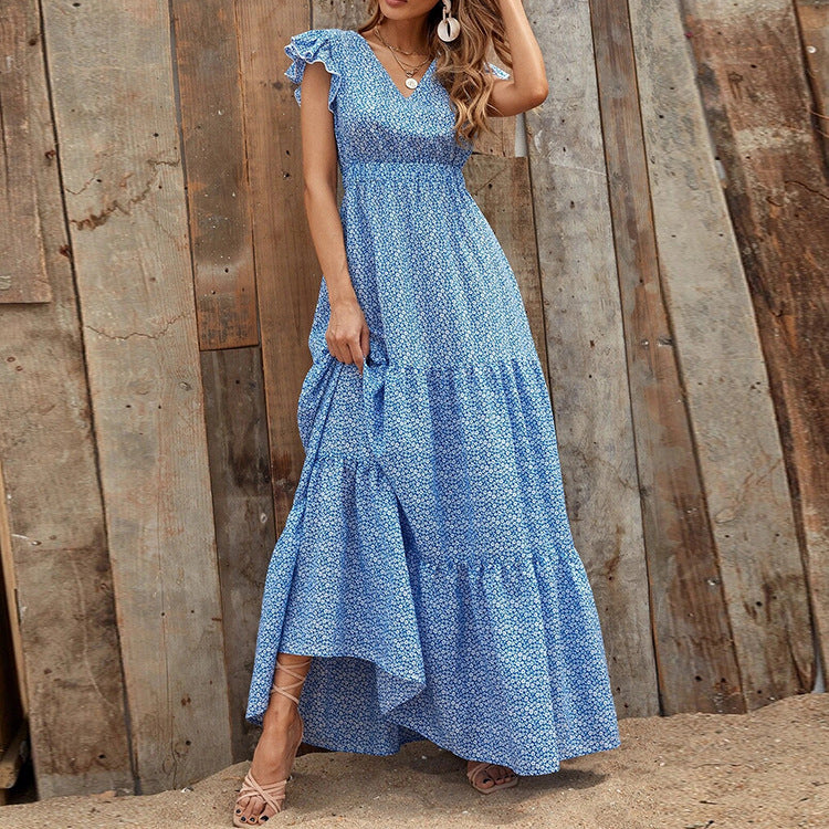 Donna con abito lungo estivo blu a fiori, in piedi su sfondo di legno rustico. Moda femminile, abbigliamento estivo elegante, stile boho chic.