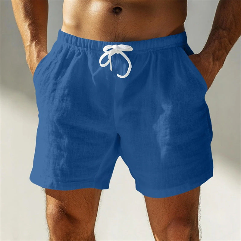 Uomo in pantaloncini blu da spiaggia, tessuto leggero, con laccio bianco in vita. Moda estiva, abbigliamento casual per mare o piscina.
