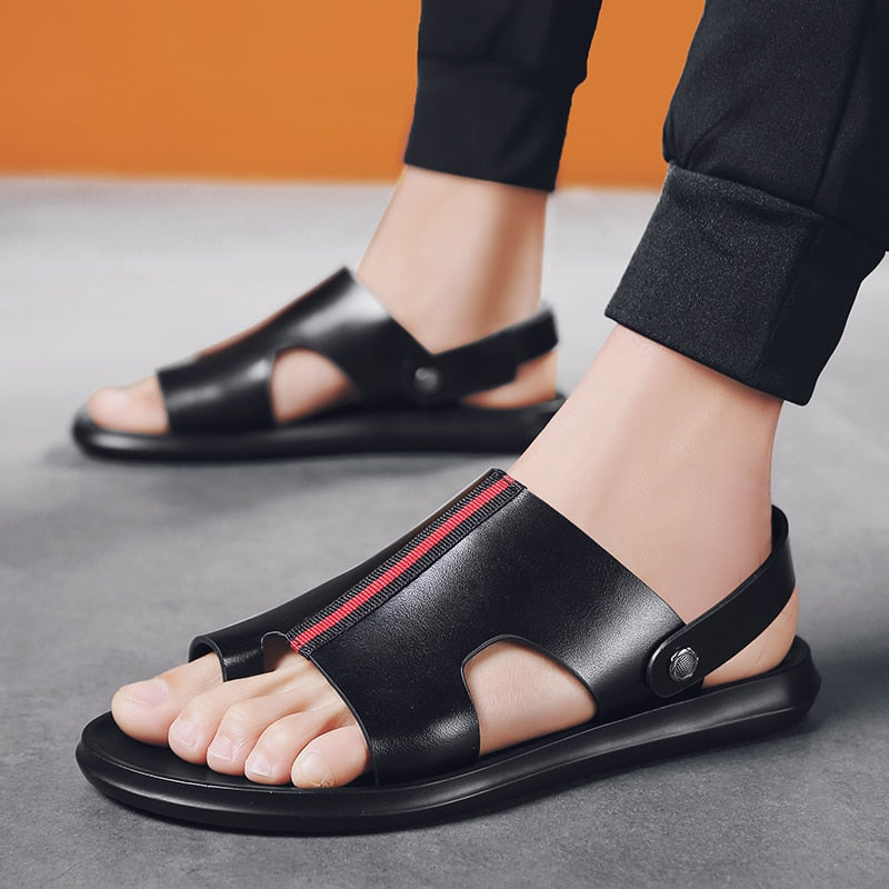 Sandali da uomo in pelle nera con design aperto, chiusura a bottone e dettaglio rosso. Calzature estive eleganti e comode su pavimento grigio.