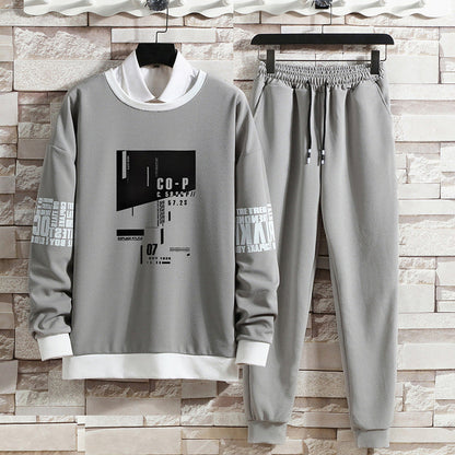 Completo tuta grigio da uomo con stampa grafica, felpa con colletto bianco e pantaloni con coulisse, appeso su sfondo di mattoni chiari.