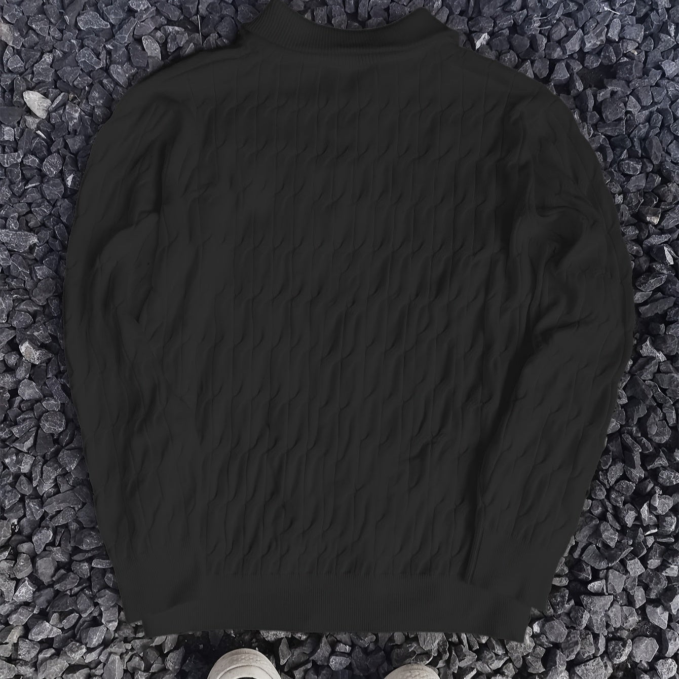 Maglione nero a trecce su sfondo di pietre grigie, moda autunno inverno, abbigliamento caldo e casual, stile elegante e confortevole.