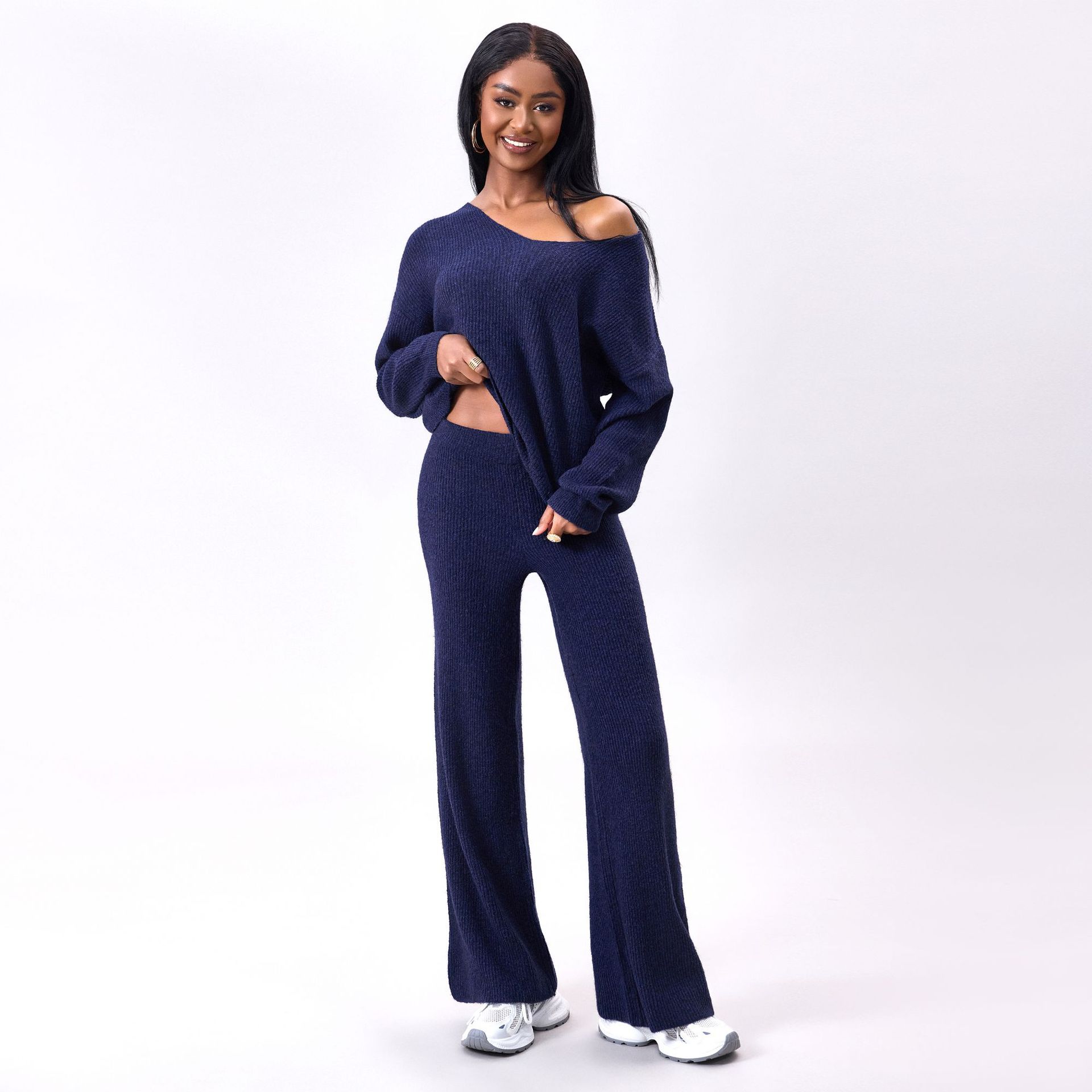 Donna sorridente in abbigliamento casual blu, maglione e pantaloni coordinati, posa su sfondo bianco. Moda donna, outfit comodo, stile autunnale.
