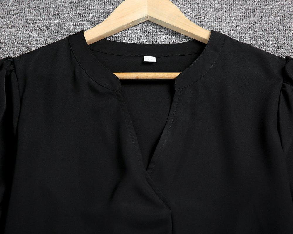 Camicia nera elegante su gruccia di legno, tessuto morbido, scollo a V, sfondo grigio. Abbigliamento moda donna, taglia media.